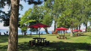 An outdoor area with picnic tables and red umbrellas, surrounded by trees and a view of the water. - Luxury bungalow in Châteauguay (Châteauguay)