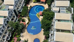 An aerial view of a resort with multiple buildings, a central swimming pool, and surrounding greenery.