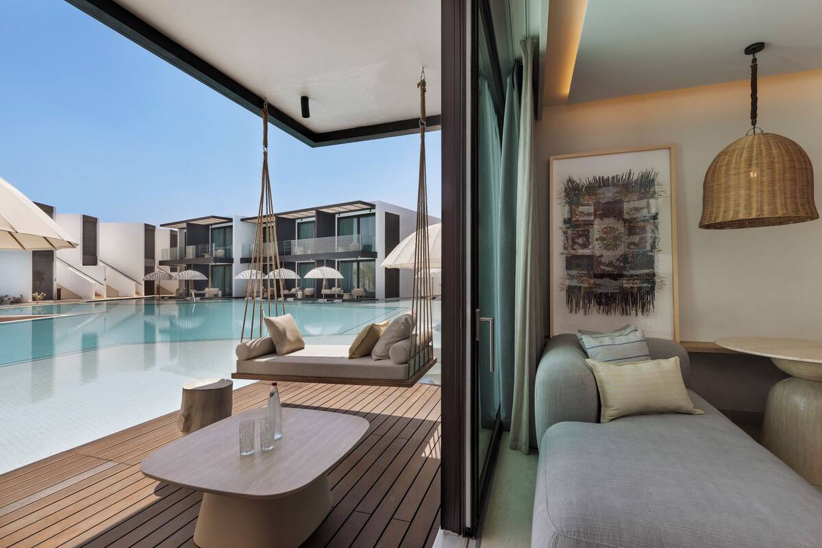 A modern outdoor lounge area with a pool, seating, and a hanging light fixture.