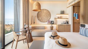 A modern hotel room with a large bed, a sitting area with a table and chairs, a view of the beach, and a minibar. - Kayma By Isrotel Exclusive (Tamar)