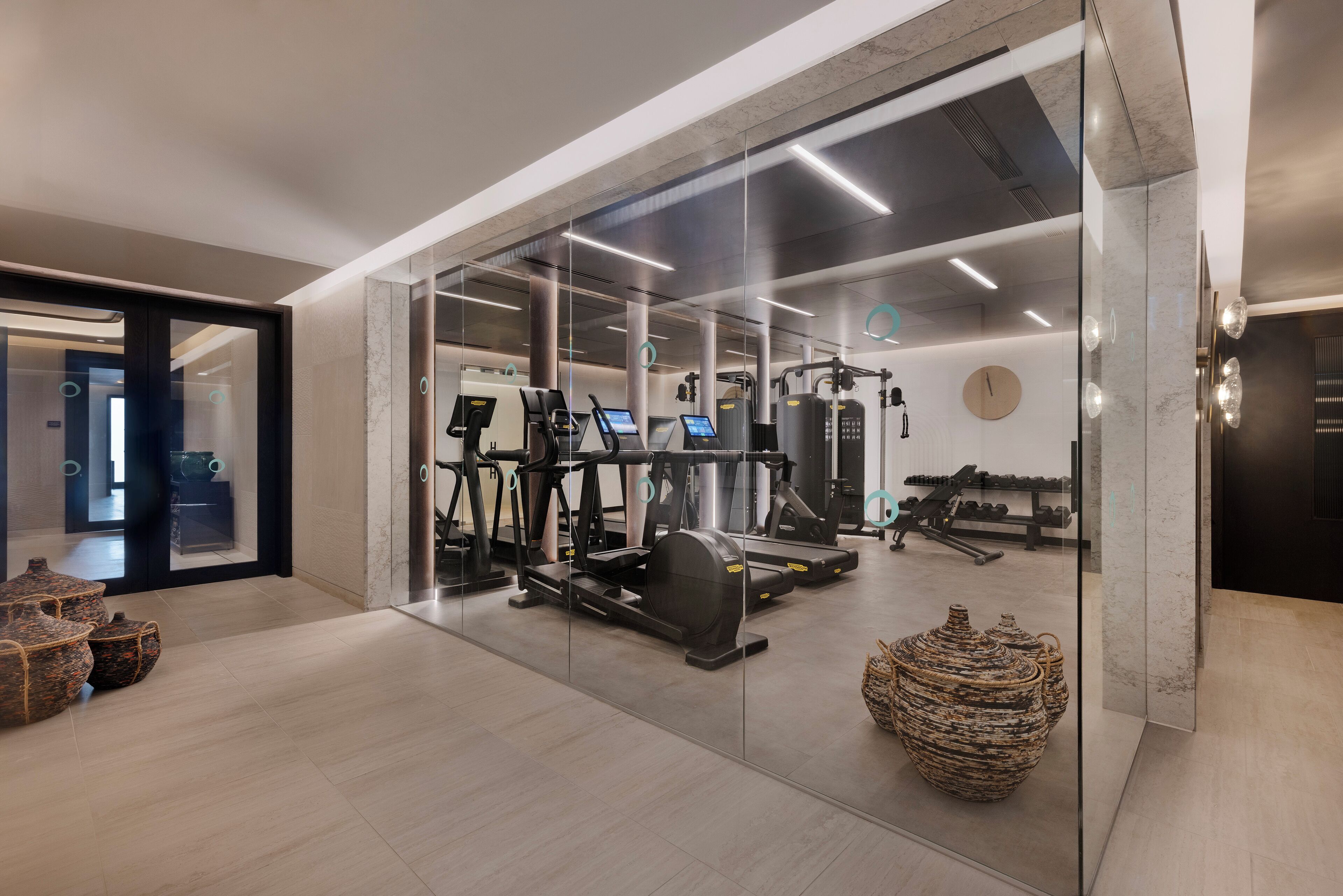 Une salle de sport moderne équipée de matériel d’exercice, dotée d’un grand miroir et d’une horloge murale.
