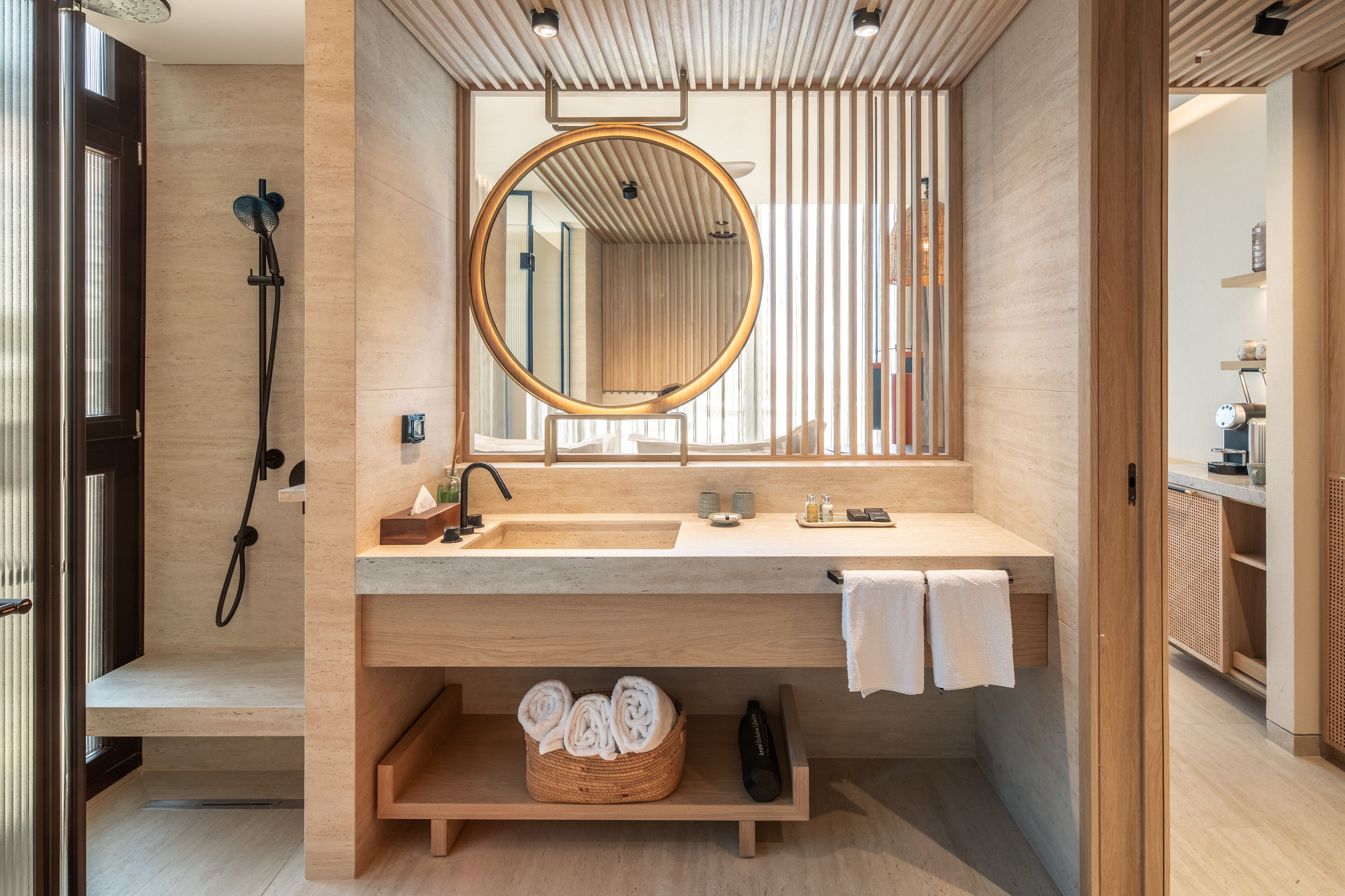 A modern bathroom with a wooden vanity, a round mirror, a built-in shower, and a shelf with towels.