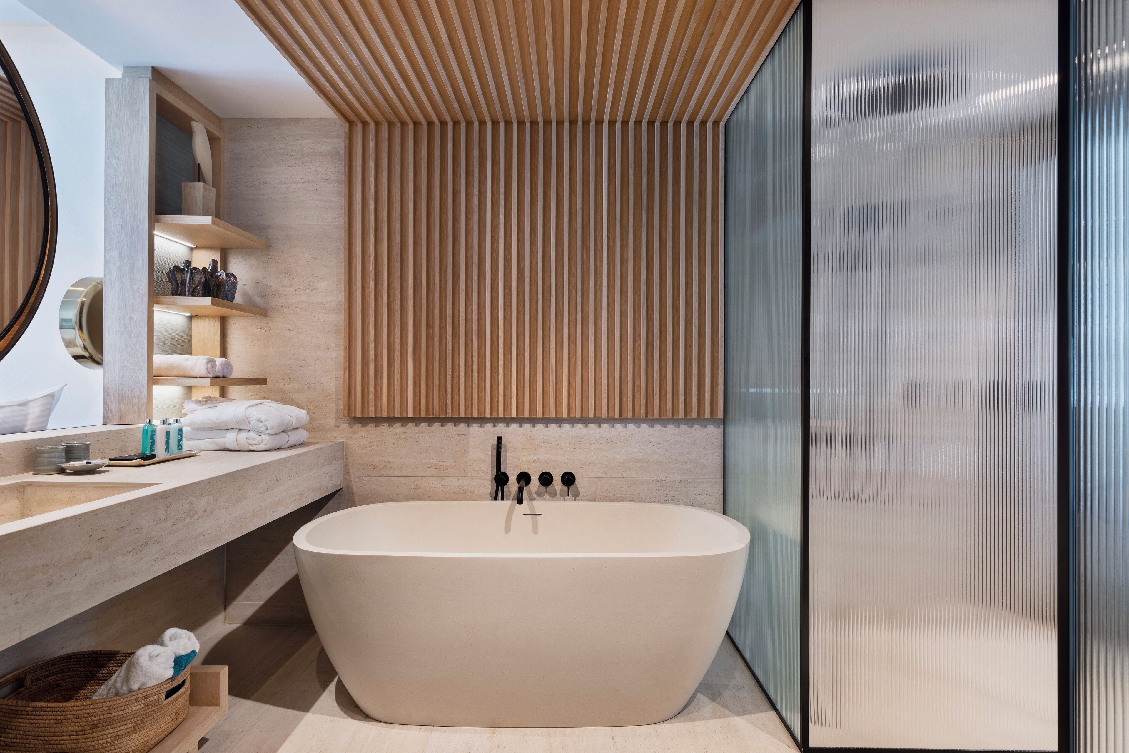A modern bathroom with a freestanding bathtub, a wooden slatted wall, and a glass shower enclosure.