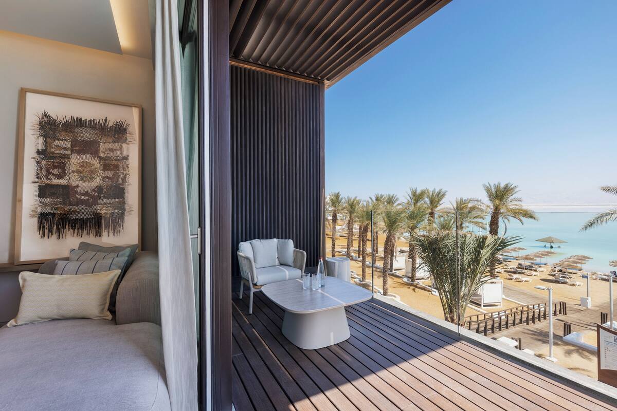 A balcony with a sofa, a table, and a view of the beach.