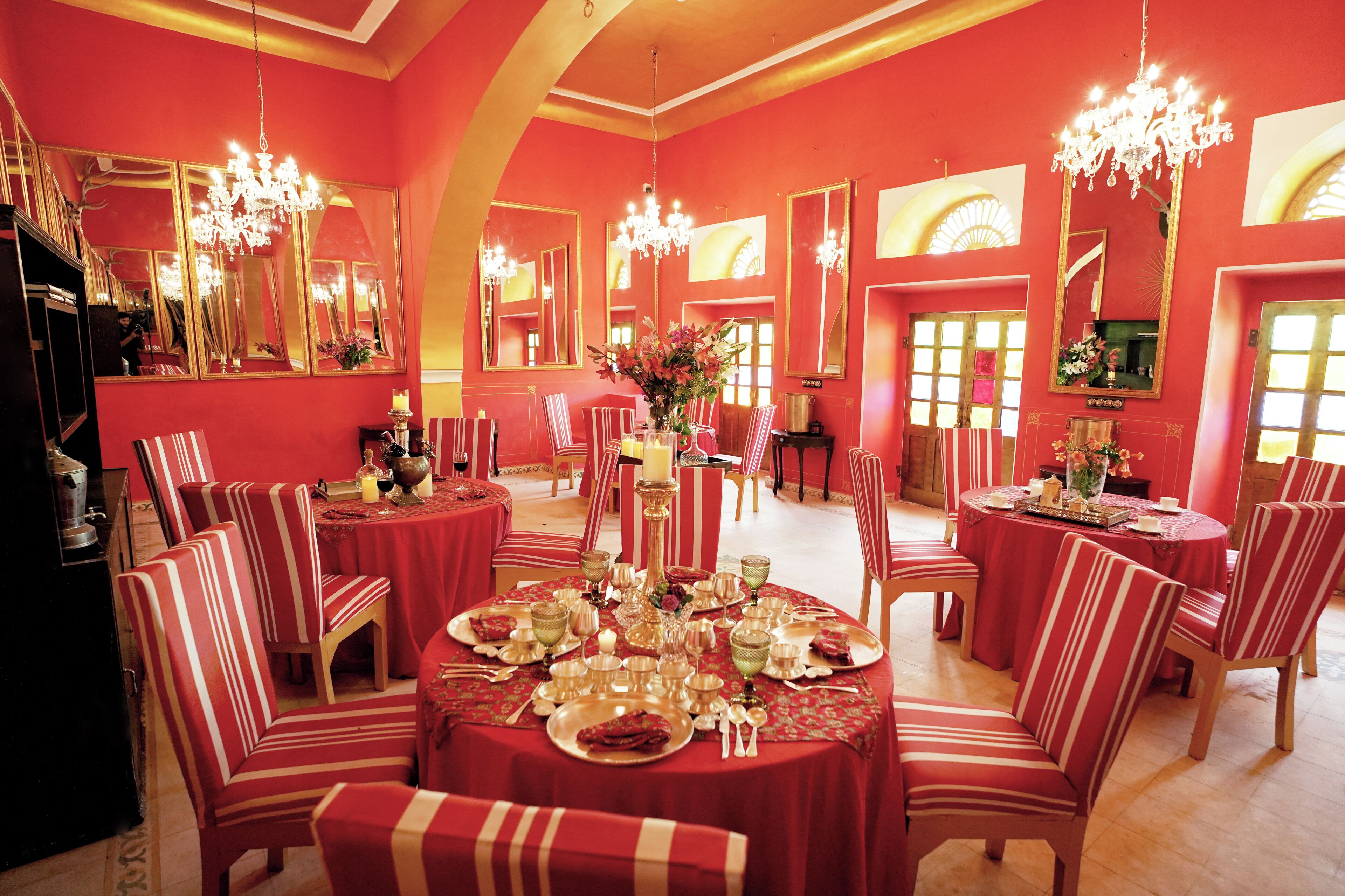 A dining area with red walls, chandeliers, and striped chairs.
