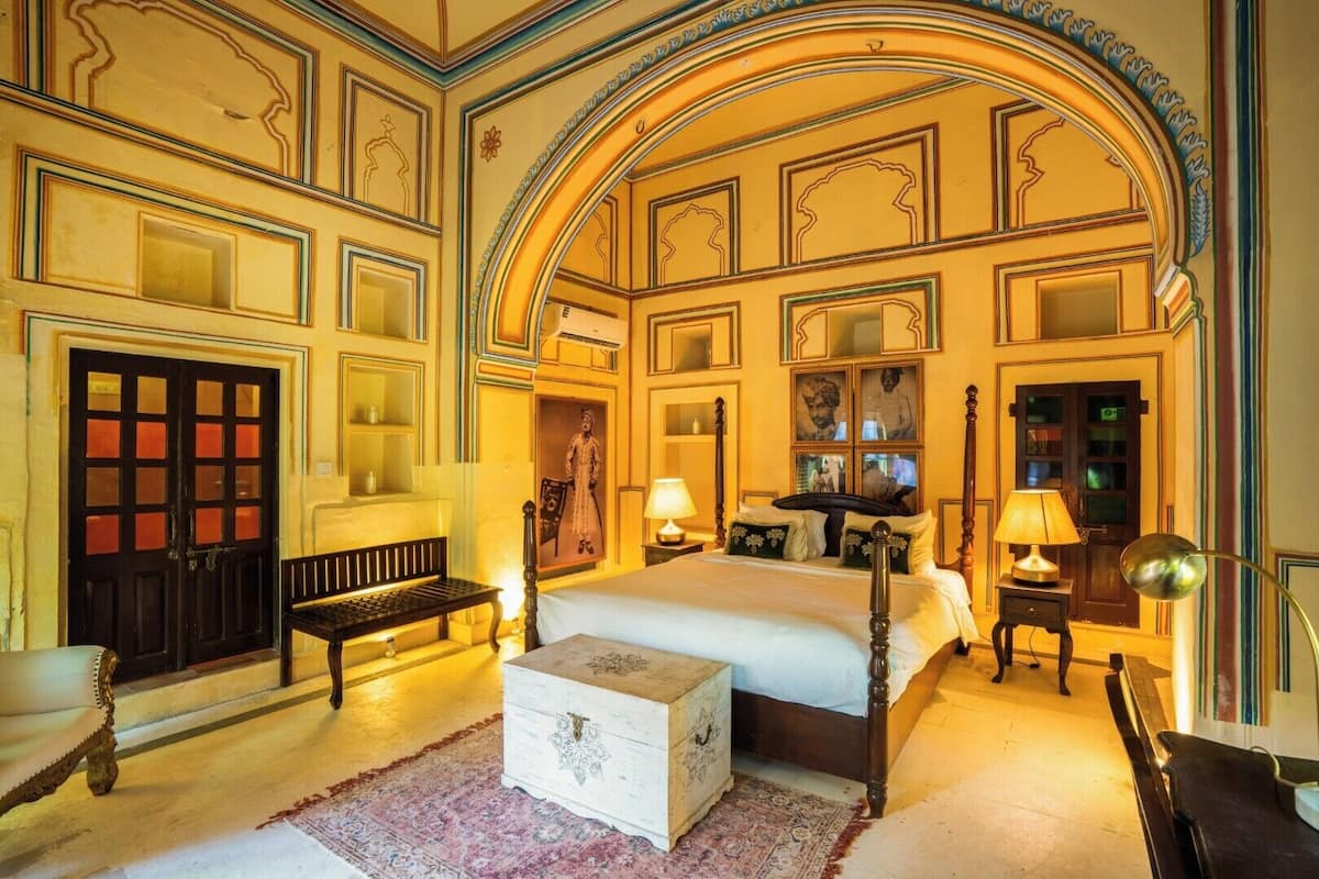 Una habitación con una cama grande, un banco, un aparador y una puerta con paneles de vidrio.