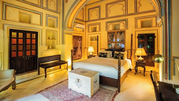 A room with a large bed, a bench, a chest of drawers, and a door with glass panels. - Medieval Forts, Kalwar, Jaipur (Jaipur)