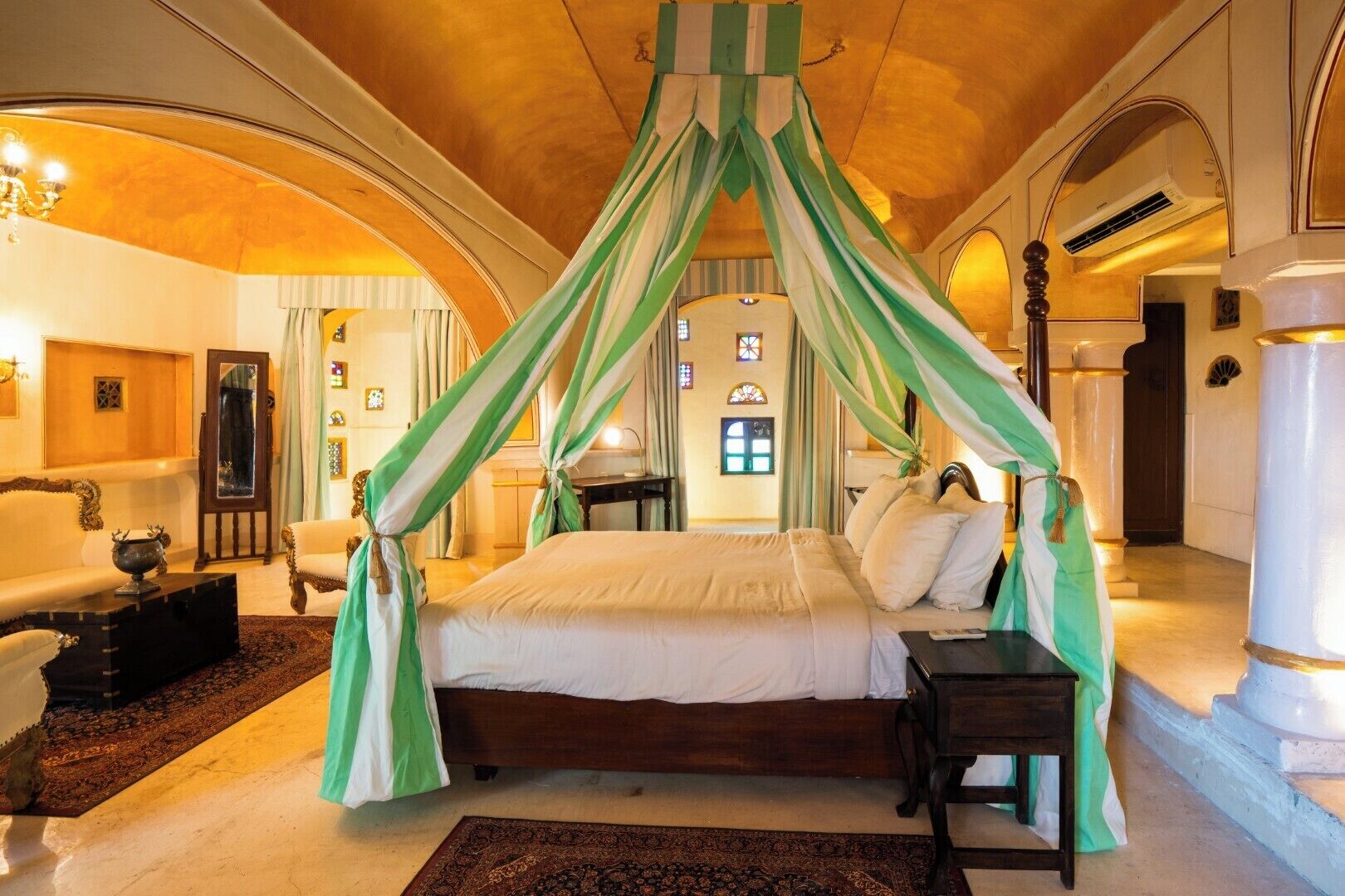 A bedroom with a canopy bed, a wooden headboard, a nightstand, and a large window with stained glass.