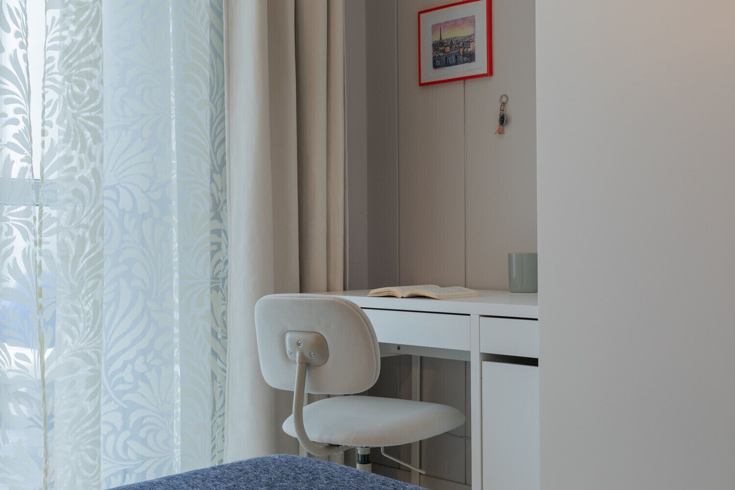 A bedroom with a bed, a desk with a chair, a window with curtains, and a picture on the wall.