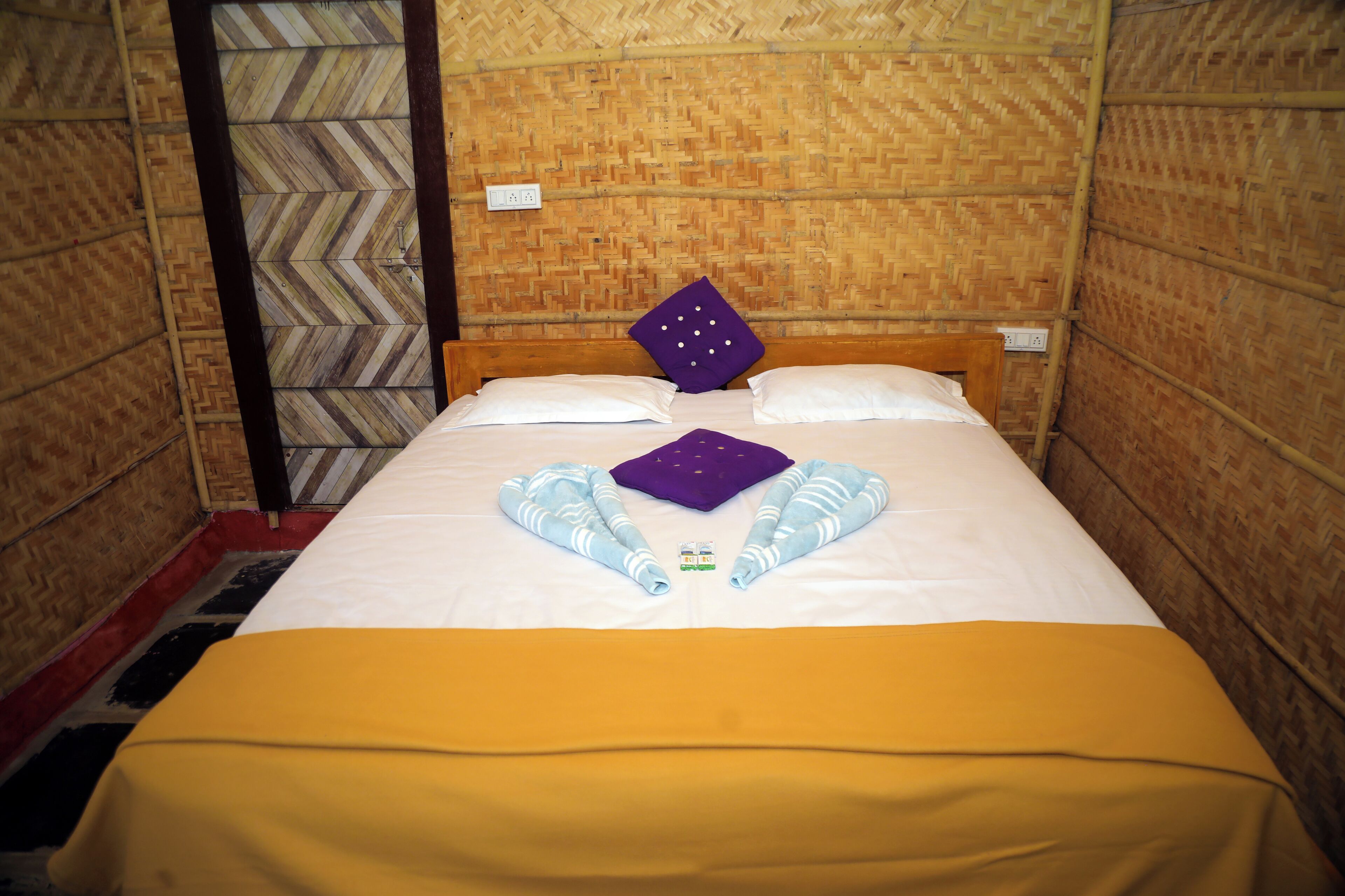 A single bed with a yellow bedspread, white pillows, and a purple pillow with white dots.