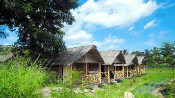 Una hilera de cabañas con techo de paja y barandillas de madera, en un paisaje verde y exuberante.