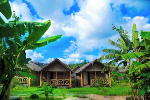A row of thatched-roof cottages with wooden railings, surrounded by lush greenery and banana trees. - Shanthi Dhama Resort (Koppal)