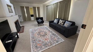 A living room with a black sofa, a patterned rug, a black chair, and a television. - Charming Cottage | Walk to City, Floriade & Eat Street (Braddon)