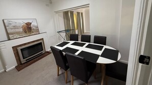 A dining area with a round table, black and white chairs, a fireplace, and a painting of a Highland cow. - Charming Cottage | Walk to City, Floriade & Eat Street (Braddon)