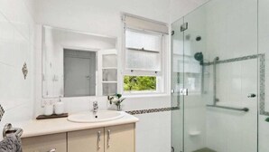 A modern bathroom with a glass-enclosed shower, a sink with a mirror above it, and a window with frosted glass. - Charming Cottage | Walk to City, Floriade & Eat Street (Braddon)