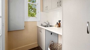 A compact kitchen with a window, a sink, and cabinets. - Charming Cottage | Walk to City, Floriade & Eat Street (Braddon)