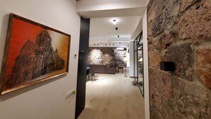 Un pasillo con pared de piedra, un cuadro de una iglesia y una zona de cocina al fondo.