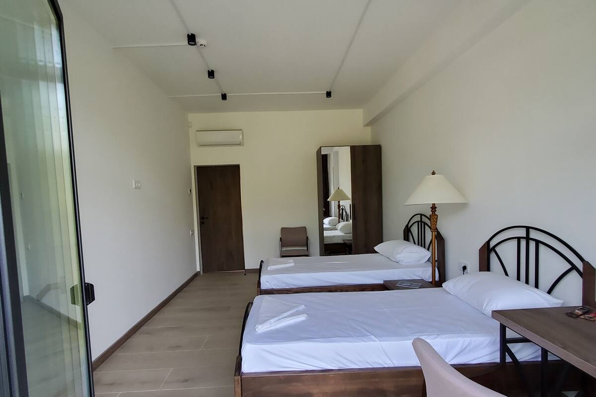 Una habitación de hotel con dos camas, un escritorio, una silla, una lámpara y un espejo.