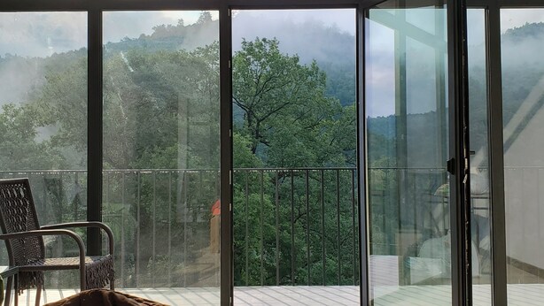 Un dormitorio con un amplio ventanal corredero que da a un balcón con vistas a una zona boscosa.