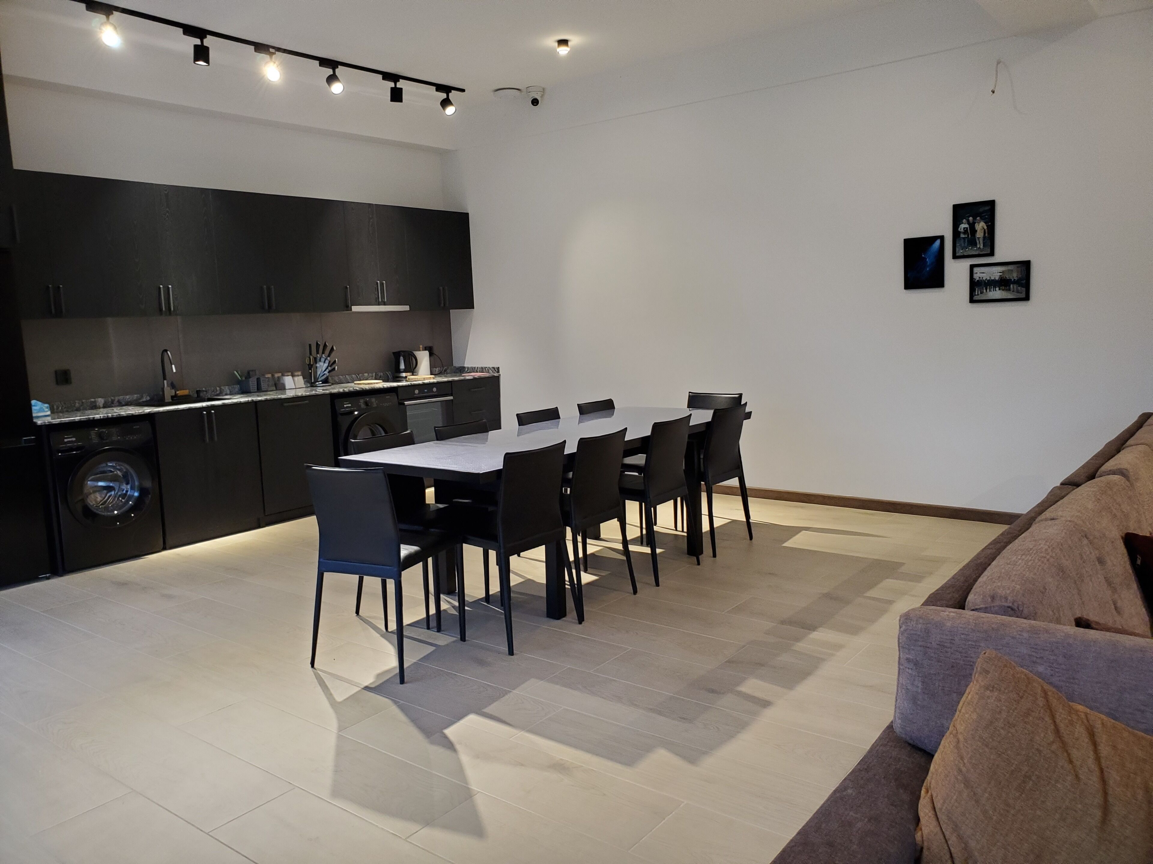 A modern kitchen with dark cabinetry, a dining table with chairs, and a sofa in a living area.