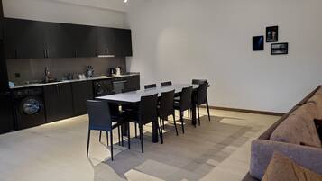 A modern kitchen with dark cabinetry, a dining table with chairs, and a sofa in a living area.