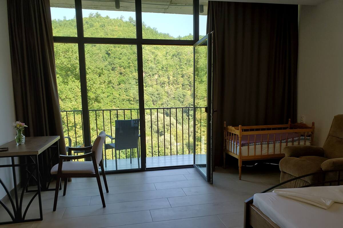 Una habitación con balcón, cama, una silla, una mesa y una mesita de noche con un florero.
