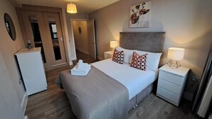 A hotel room with a large bed, two bedside tables, a wardrobe, and a door leading to a bathroom.
