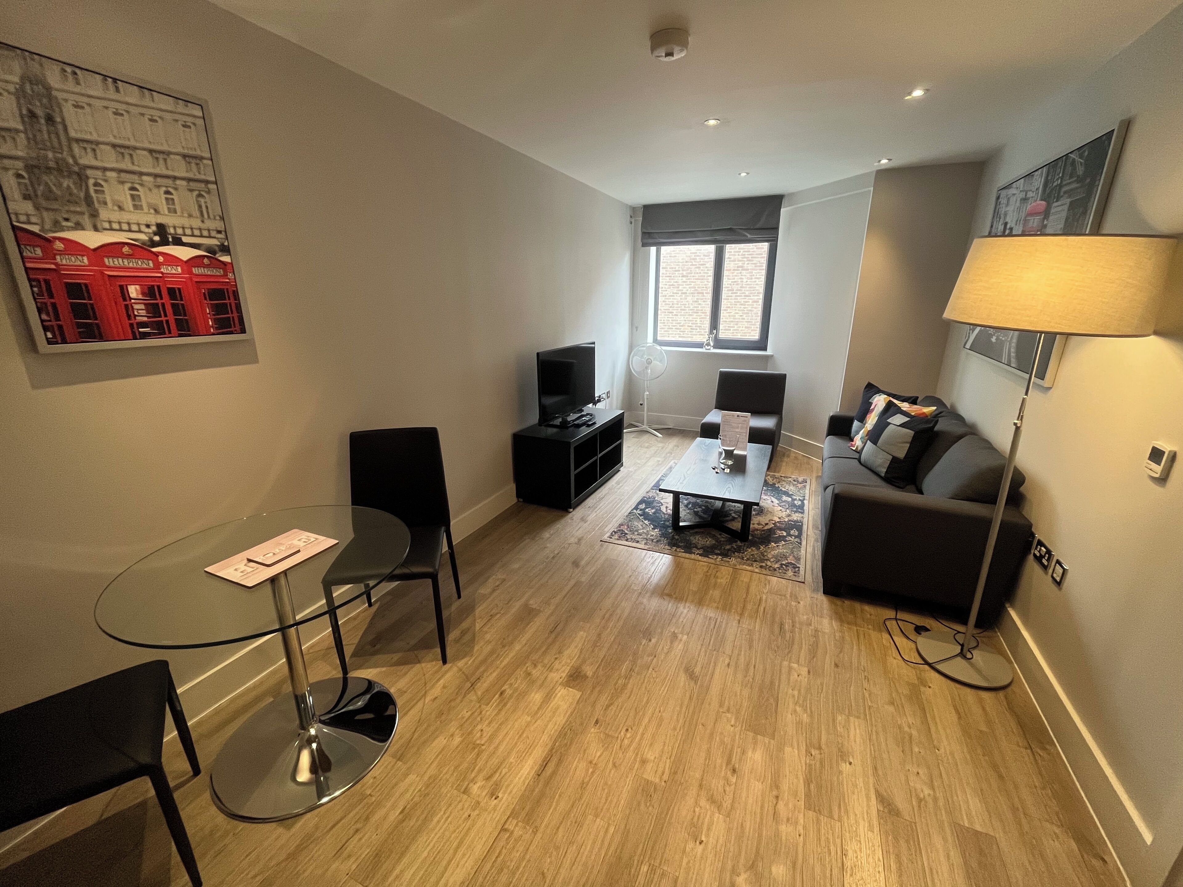 Ein modernes Wohnzimmer mit Glastisch, schwarzen Stühlen, einer Couch, einem Fernseher und einer Lampe.