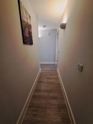 Un couloir doté d’un plancher en bois, de murs blancs et d’un tableau accroché sur le mur de gauche.