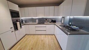 A modern kitchen with white cabinets, a wooden floor, and a stainless steel sink.