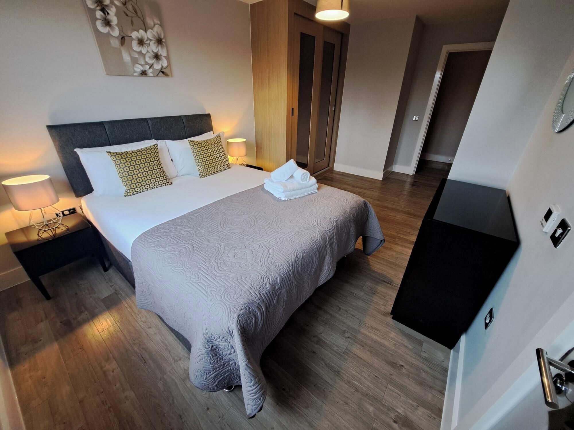 A hotel room with a large bed, two bedside lamps, a wooden floor, a wardrobe, and a TV.