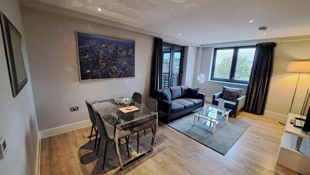 A modern living room with a glass dining table, a sofa, and a coffee table. There is a large window with curtains and a cityscape view.