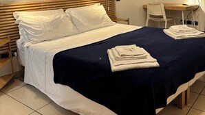 A neatly made bed with white linens, a dark blue bedspread, and folded towels on the side. - Dimora della Posta (Mondovì)