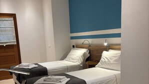 A hotel room with two beds, a wooden table, and a desk with a lamp. - Dimora della Posta (Mondovì)