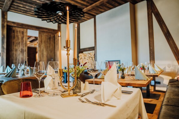A dining table set with wine glasses, cutlery, and candles, in a room with wooden beams and a white tablecloth. - WALDGUT Naturresort (Bad Gottleuba-Berggiesshuebel)