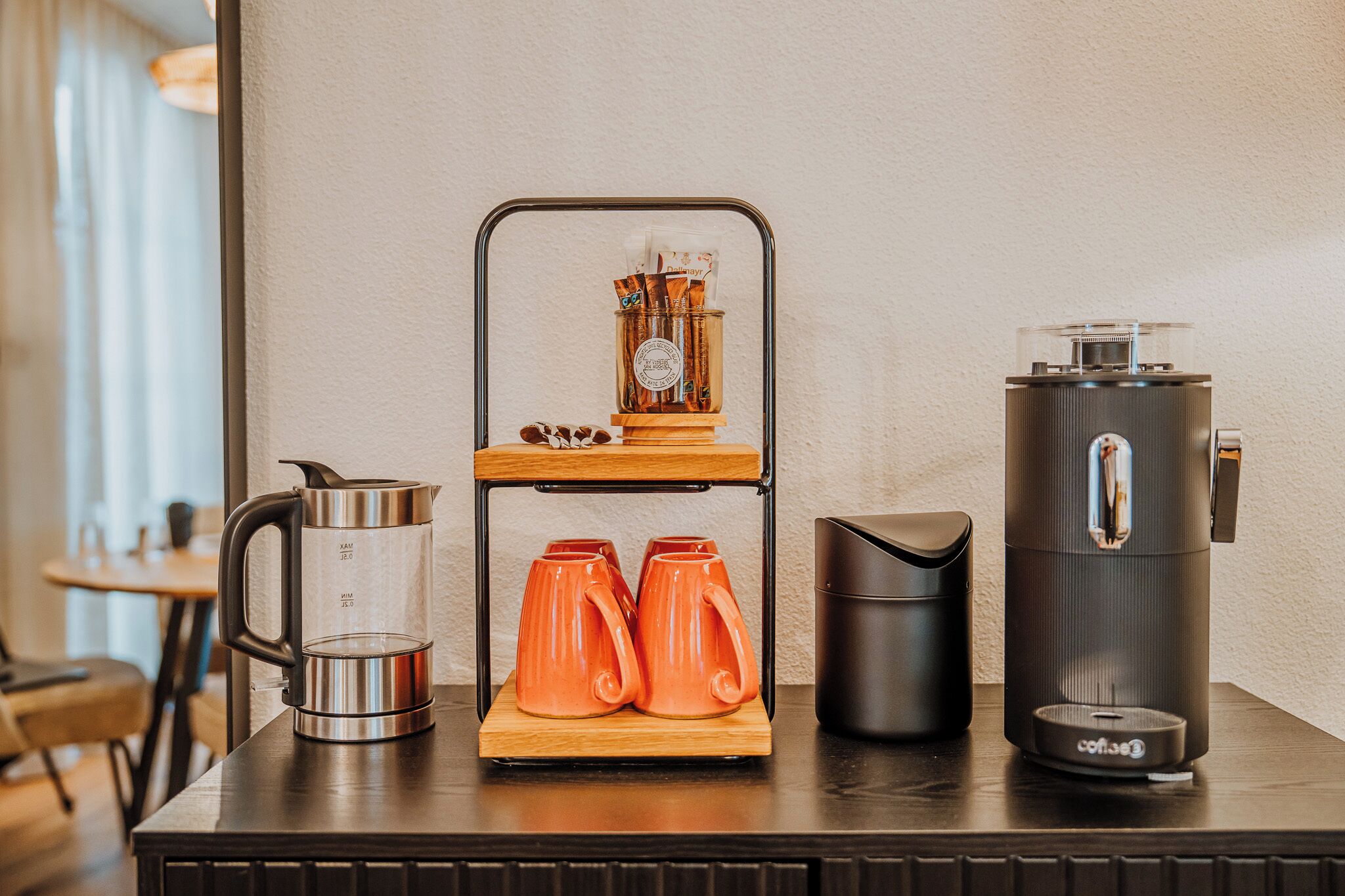 Eine Kaffeestation mit einer Kaffeemaschine, einer Kaffeemühle und zwei orangefarbenen Tassen auf einem Holzständer.