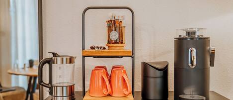 A coffee station with a coffee maker, a grinder, and two orange mugs on a wooden stand.