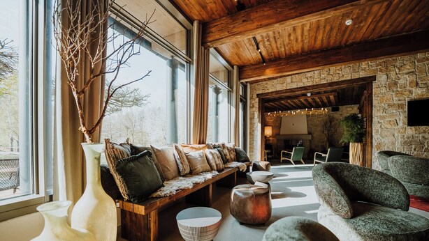 A modern interior with a stone wall, wooden ceiling, and a seating area with a bench and chairs. - WALDGUT Naturresort (Bad Gottleuba-Berggiesshuebel)