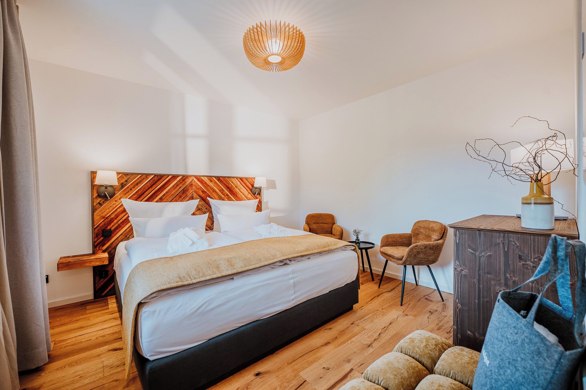 A modern hotel room with a large bed, a wooden headboard, a desk, and a chair.