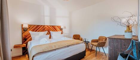 A modern hotel room with a large bed, a wooden headboard, a desk, and a chair.