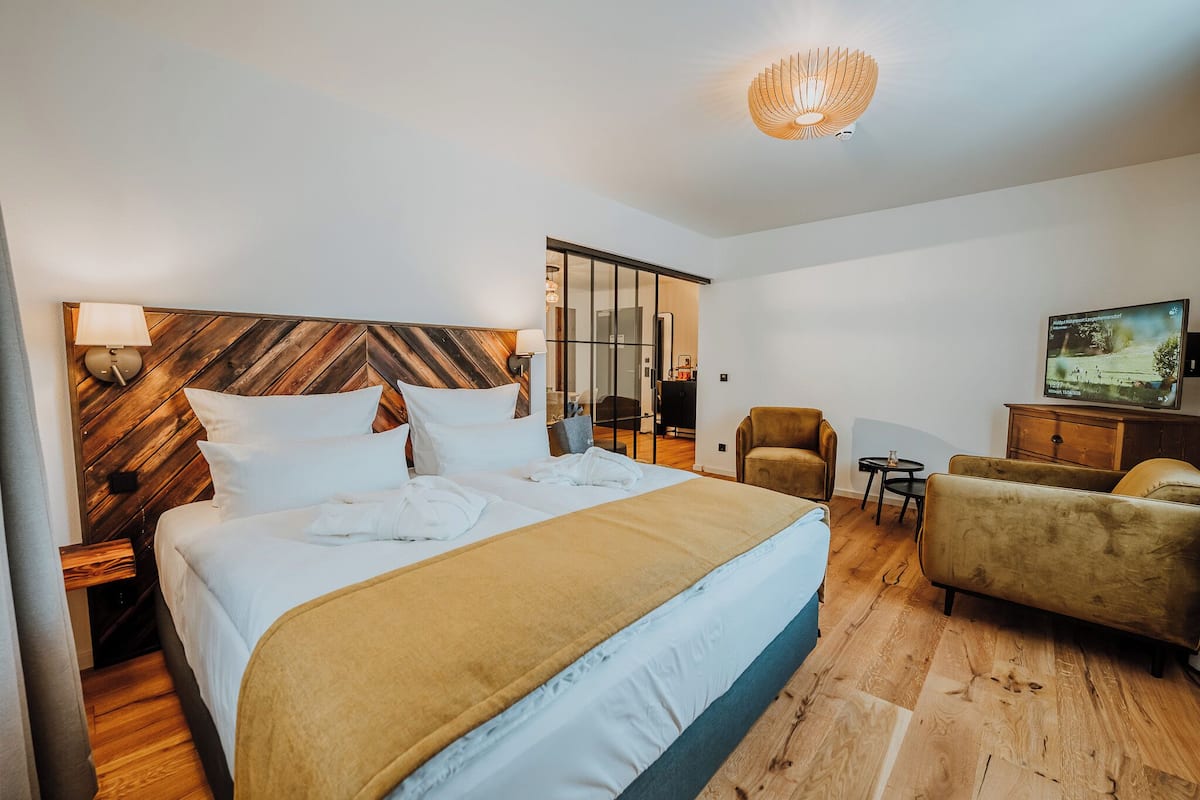 A hotel room with a large bed, a wooden headboard, a sofa, a TV, and a small table.