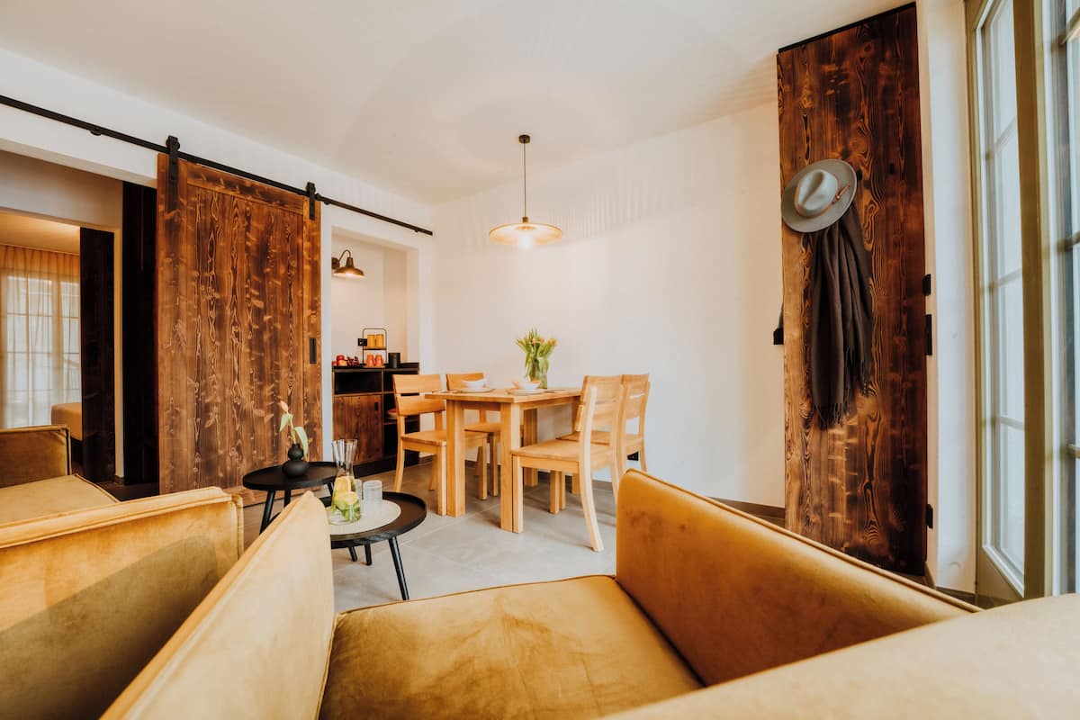 A modern living room with a sofa, a dining table with chairs, a hanging light fixture, and a sliding barn door.