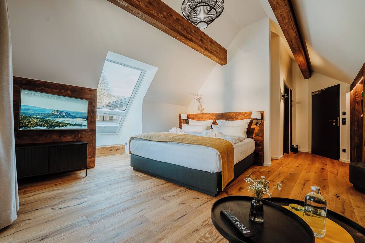A bedroom with a bed, a TV, a wooden floor, and a window.