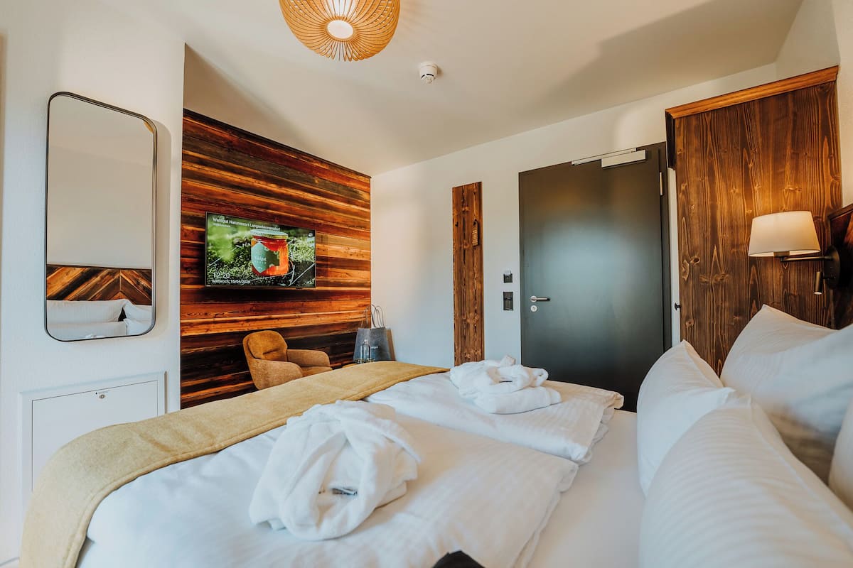 A hotel room with a bed, a wooden wall panel, a television, a door, and a lamp.