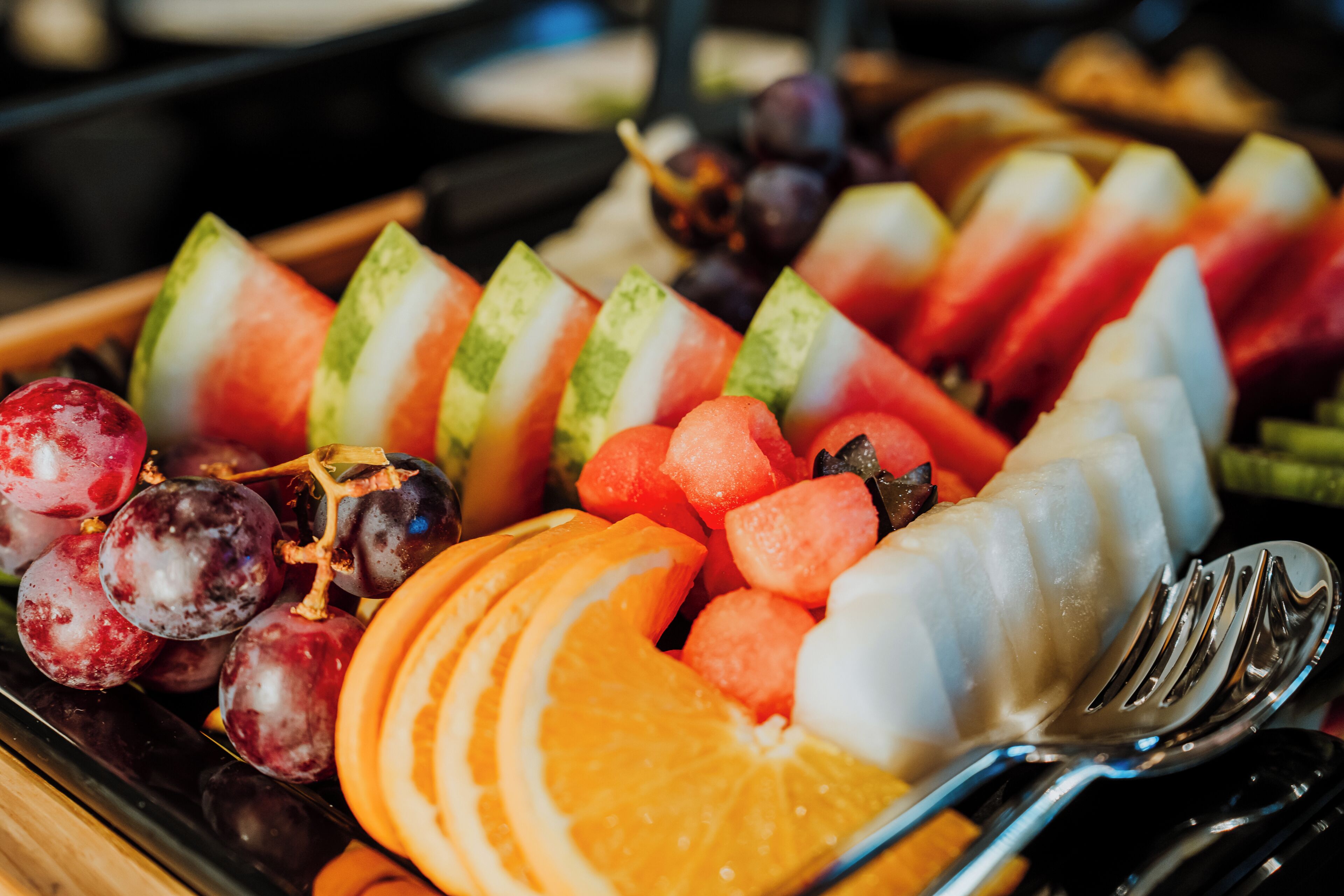 A fruit platter with sliced watermelon, cantaloupe, grapes, and orange segments.