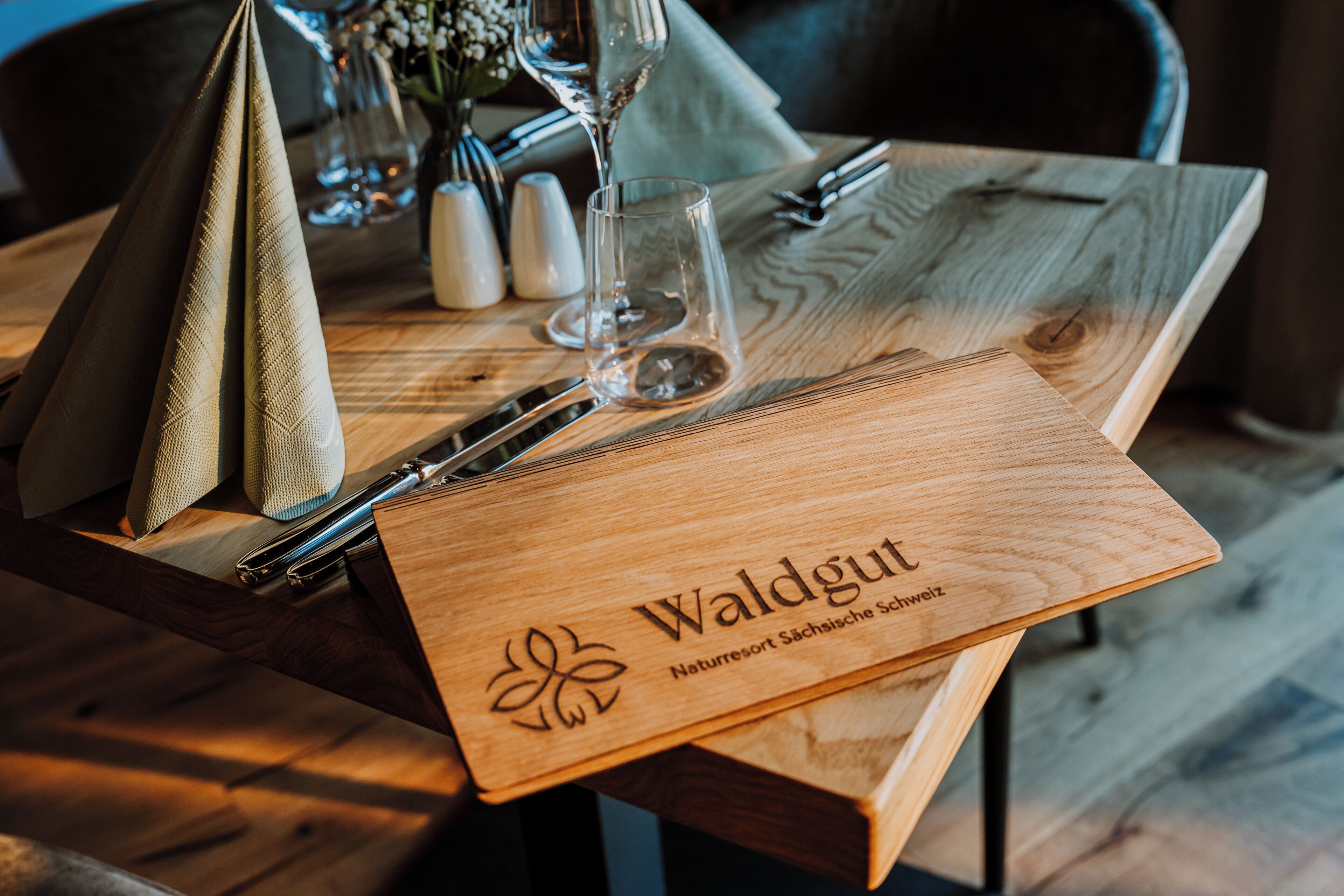 Una mesa de madera con un menú, cubiertos y una copa.