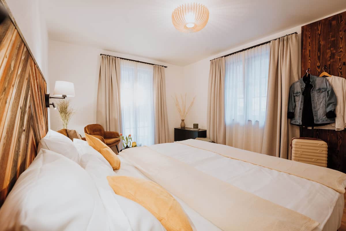 A hotel room with a large bed, a desk, a chair, a hanging jacket, and a lamp.