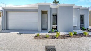 Una casa moderna de dos pisos con garaje, puerta principal y un pequeño porche con plantas.