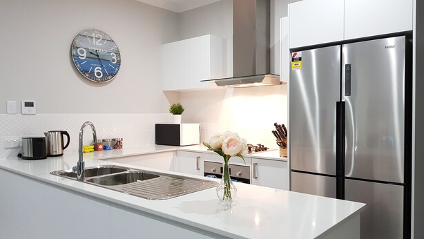 Una cocina moderna con armarios blancos, electrodomésticos de acero inoxidable, un reloj y un florero con flores en la encimera.