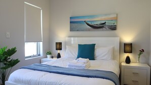 A neatly made bed with a blue blanket, white pillows, and a painting of a boat on the wall. - Culloton Escape – Spacious 3BR Family Home Near Parks & Shops (Balga)